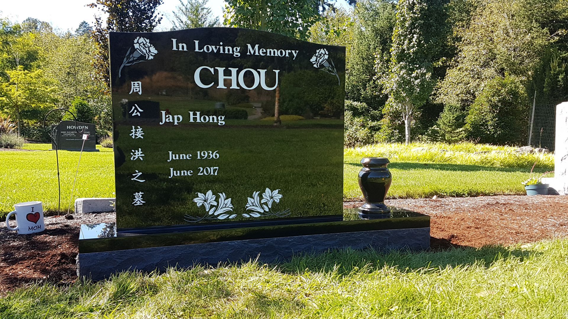 a black gravestone with the name chou on it in a cemetery .