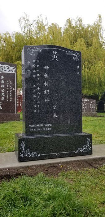 a large black gravestone in a cemetery with chinese writing on it .