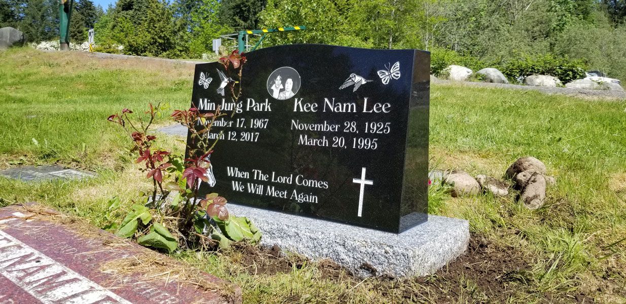 A black gravestone with a cross on it is in a cemetery.
