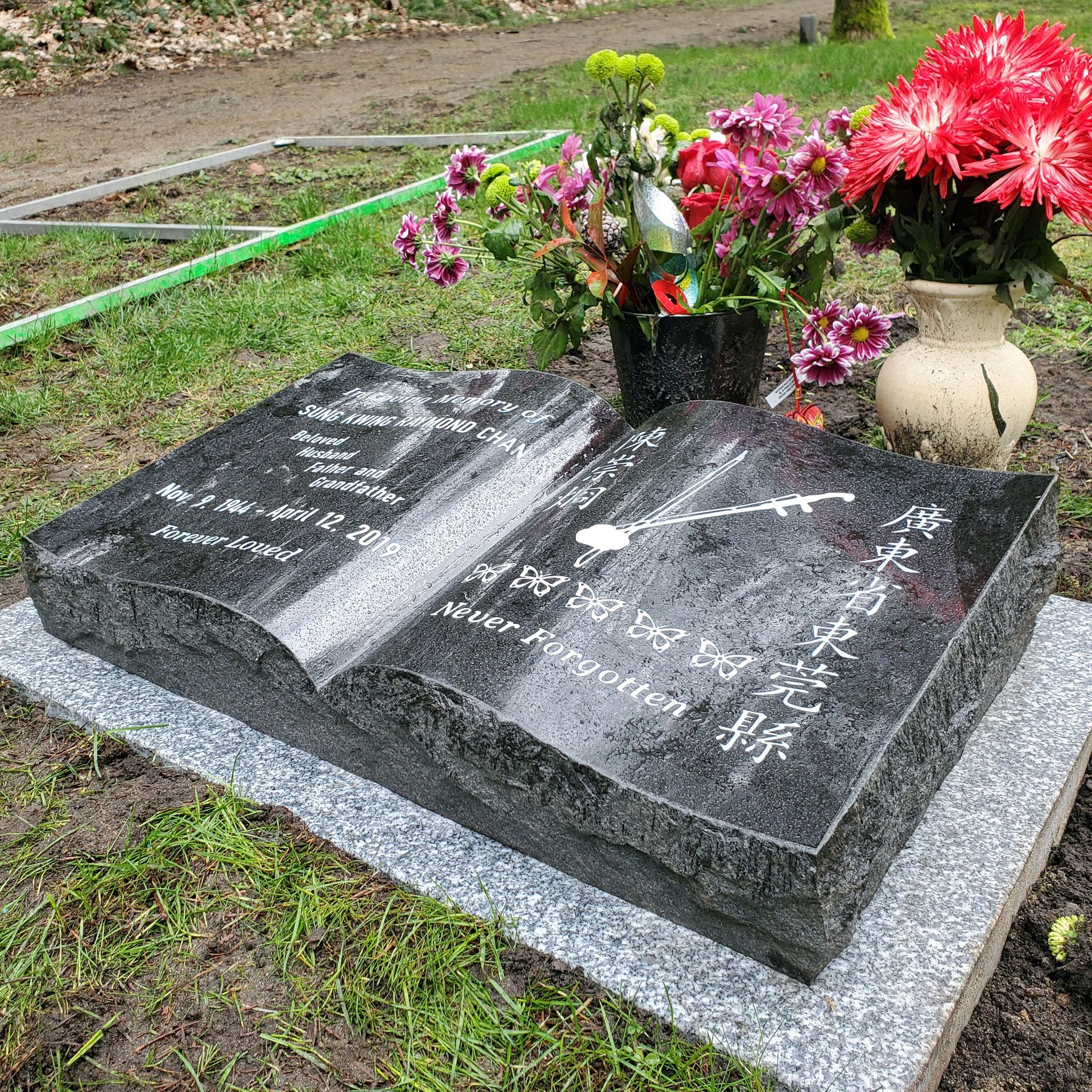 A grave with flowers in vases on it in a cemetery.