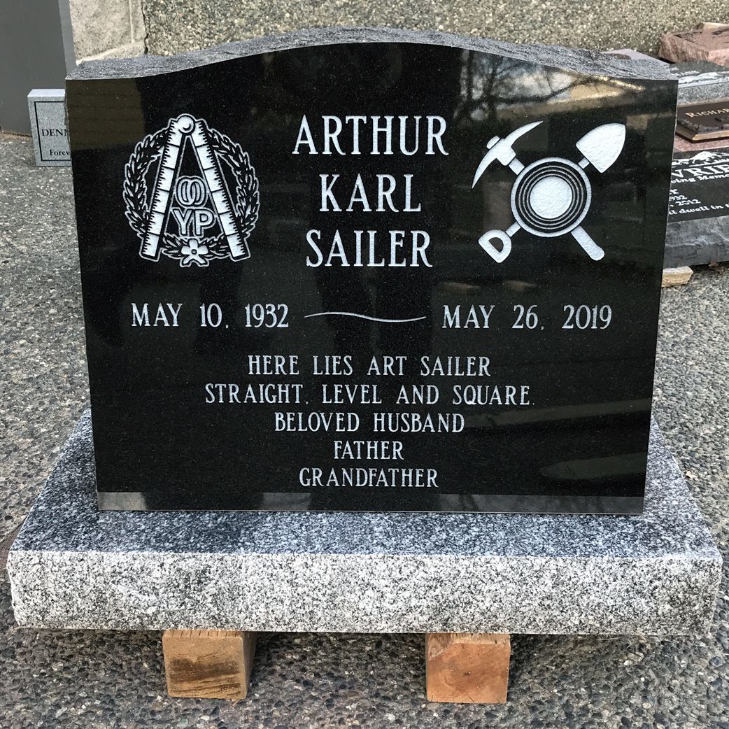 a black gravestone for arthur karl sailer is sitting on top of a wooden bench .
