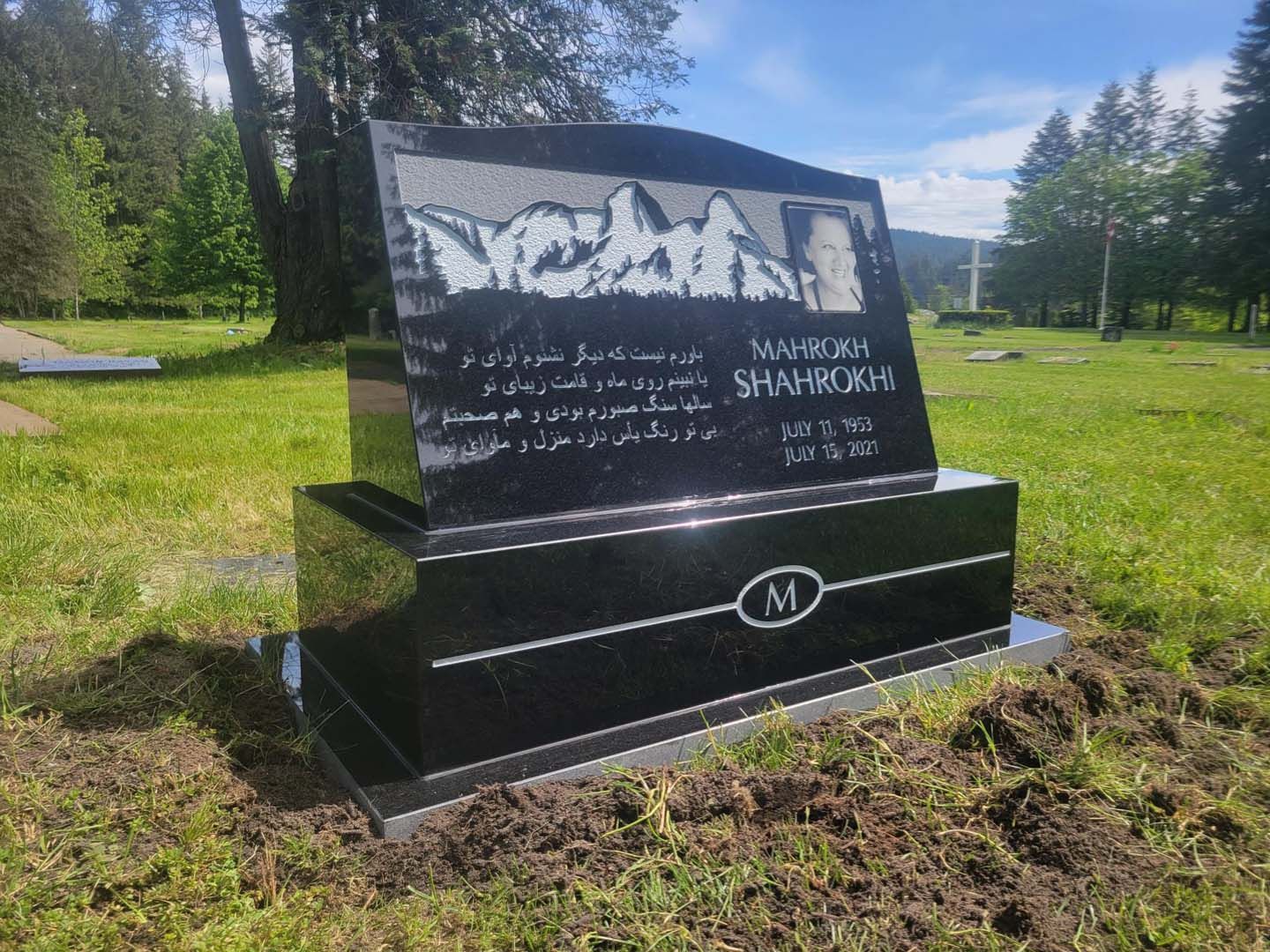 a black gravestone is sitting in the middle of a grassy field .