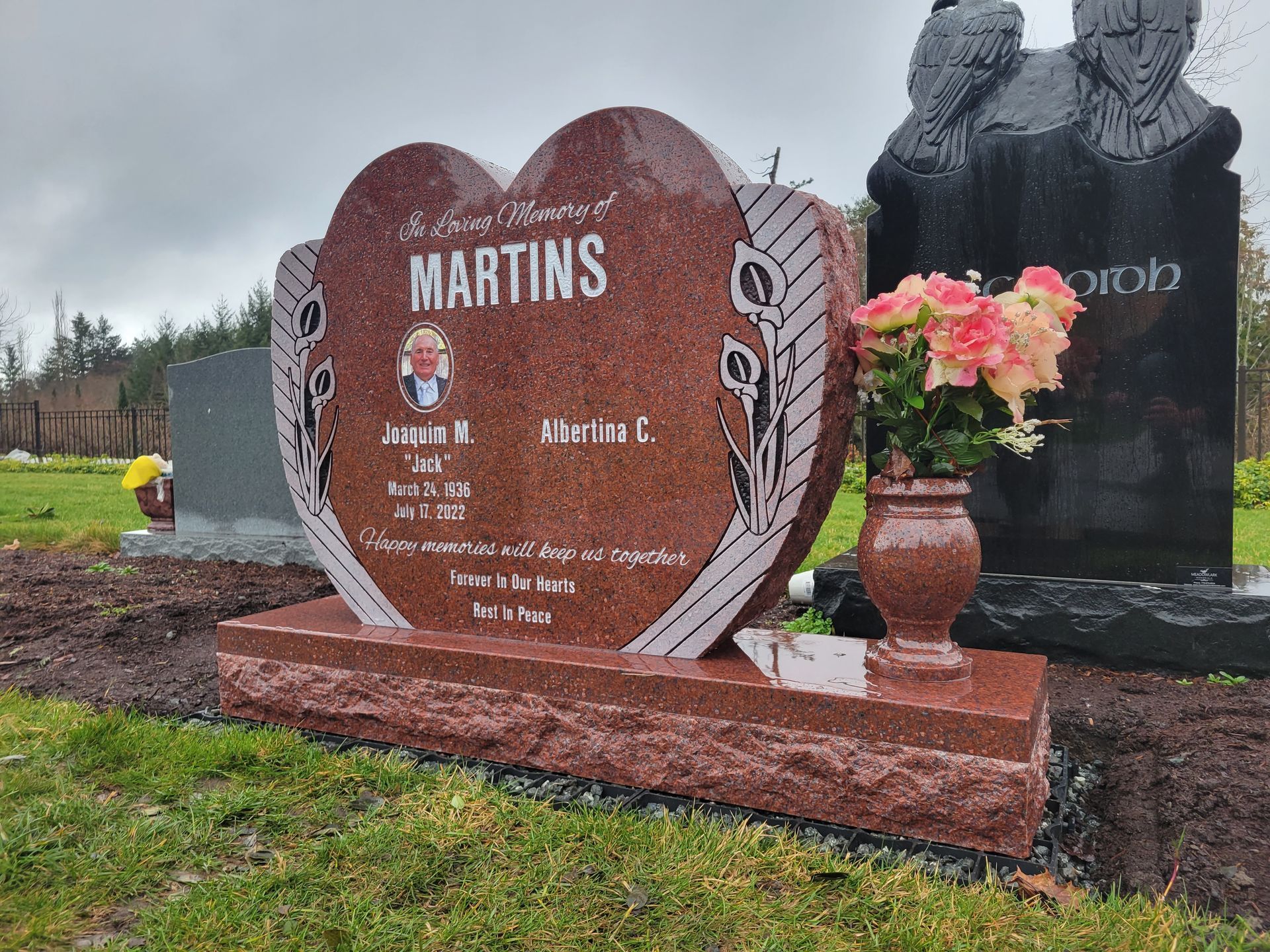 a heart shaped gravestone in a cemetery with flowers in a vase .