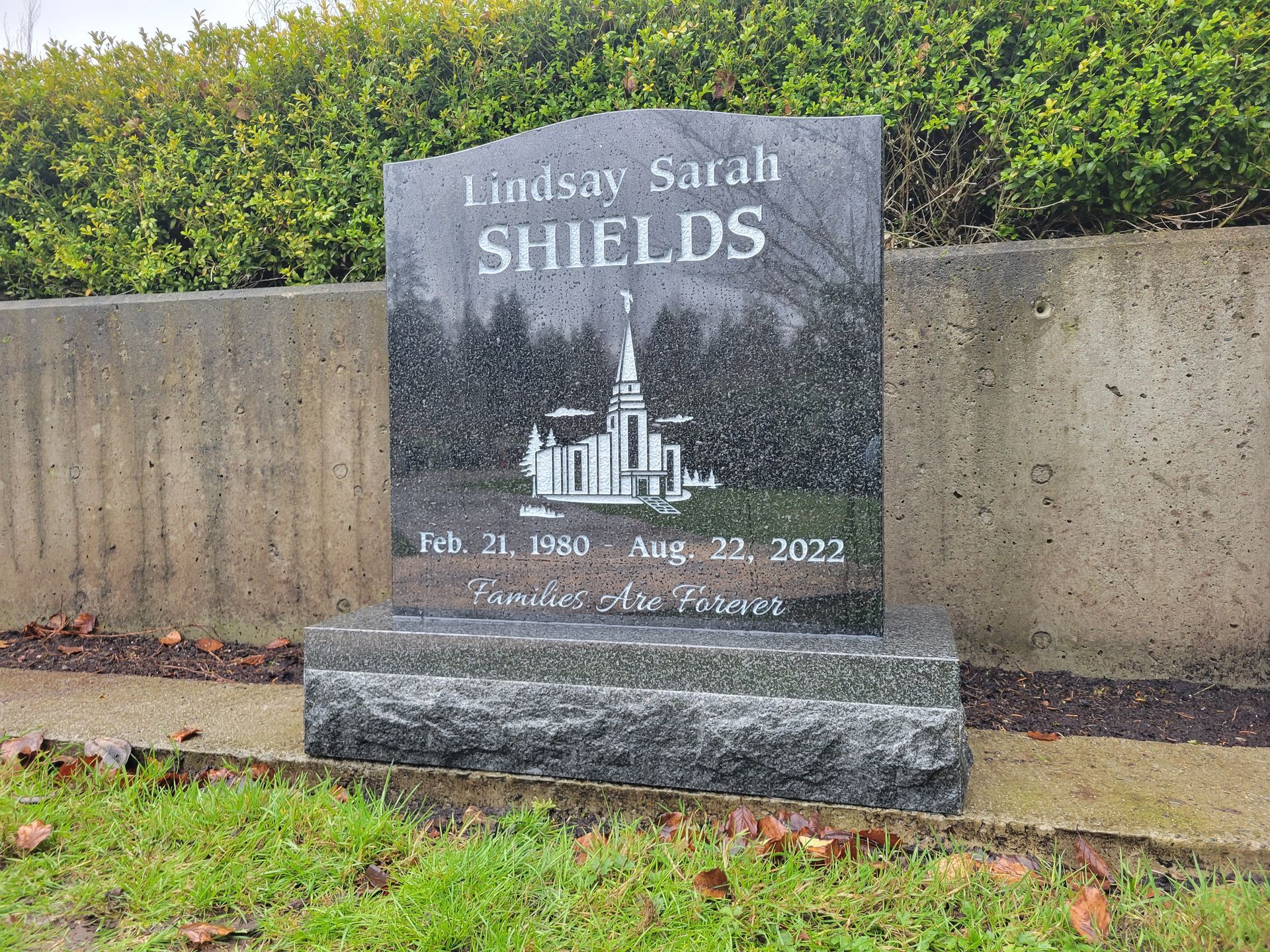 a gravestone for lindsay sarah shields is sitting in the grass next to a wall .