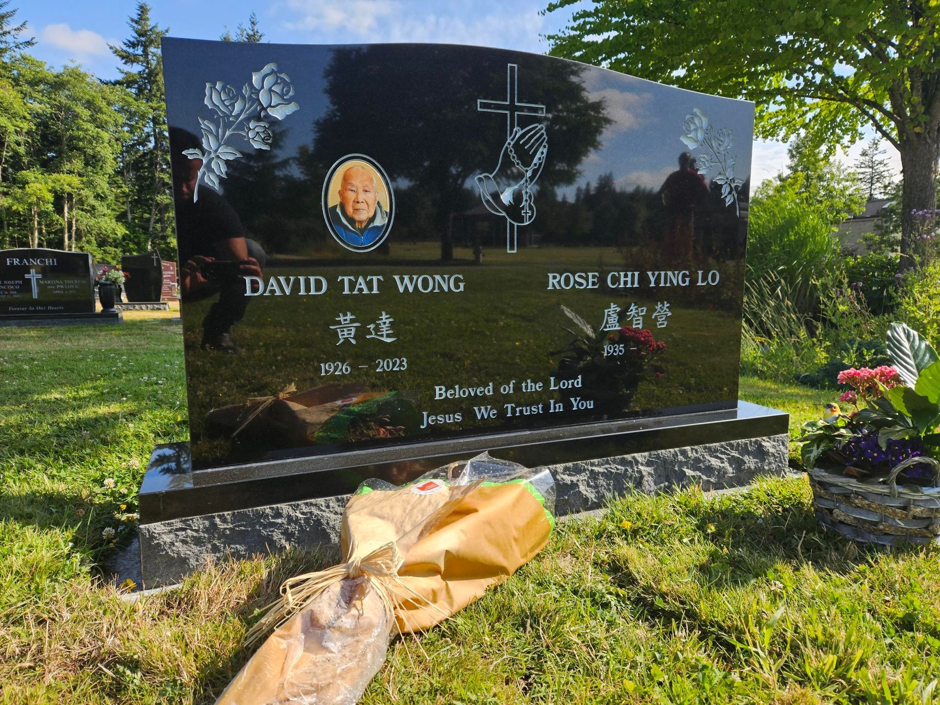 a black head stone with a cross and roses on it is in a grassy field
