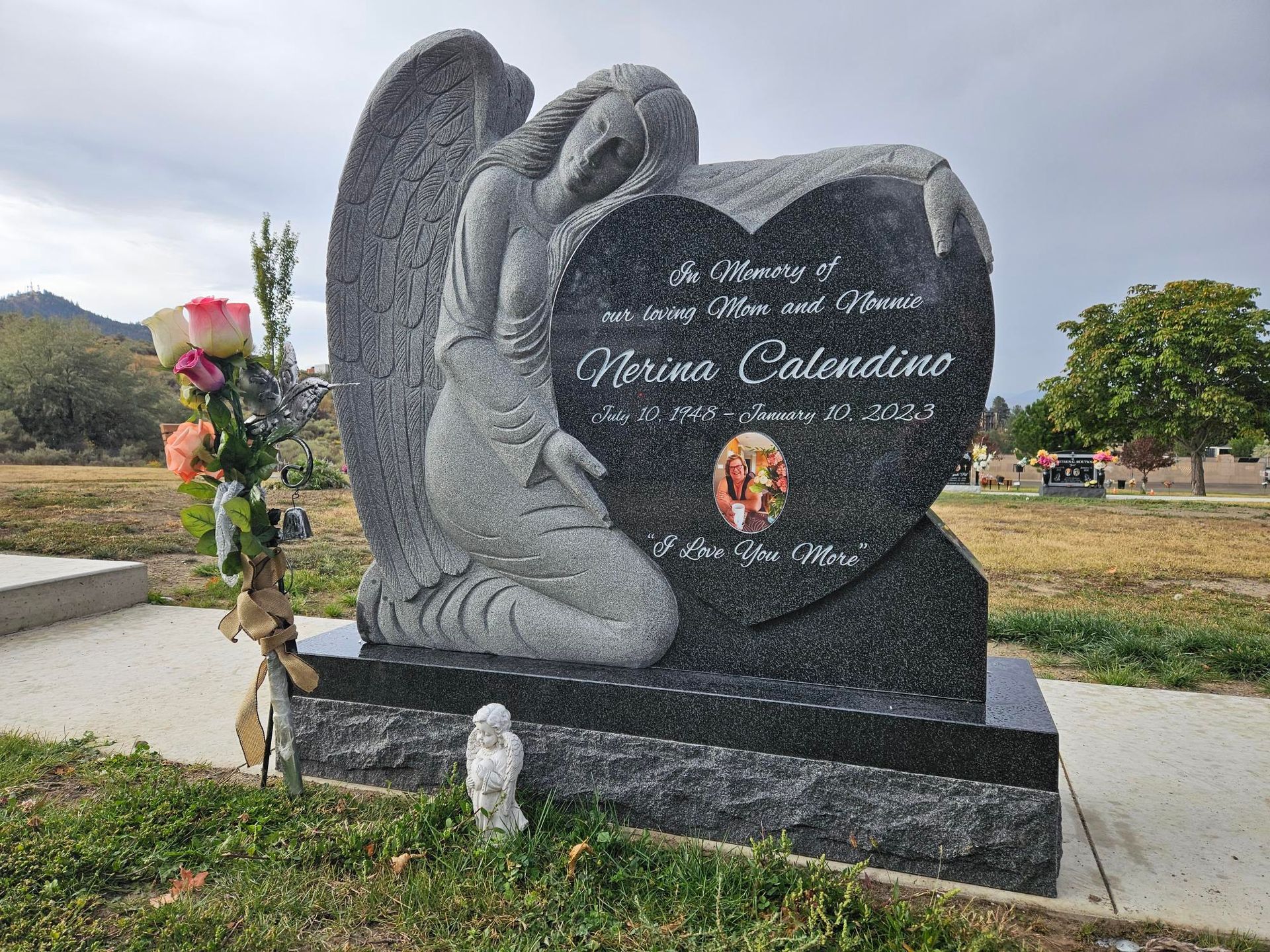 a gravestone with a statue of an angel holding a heart in a cemetery .