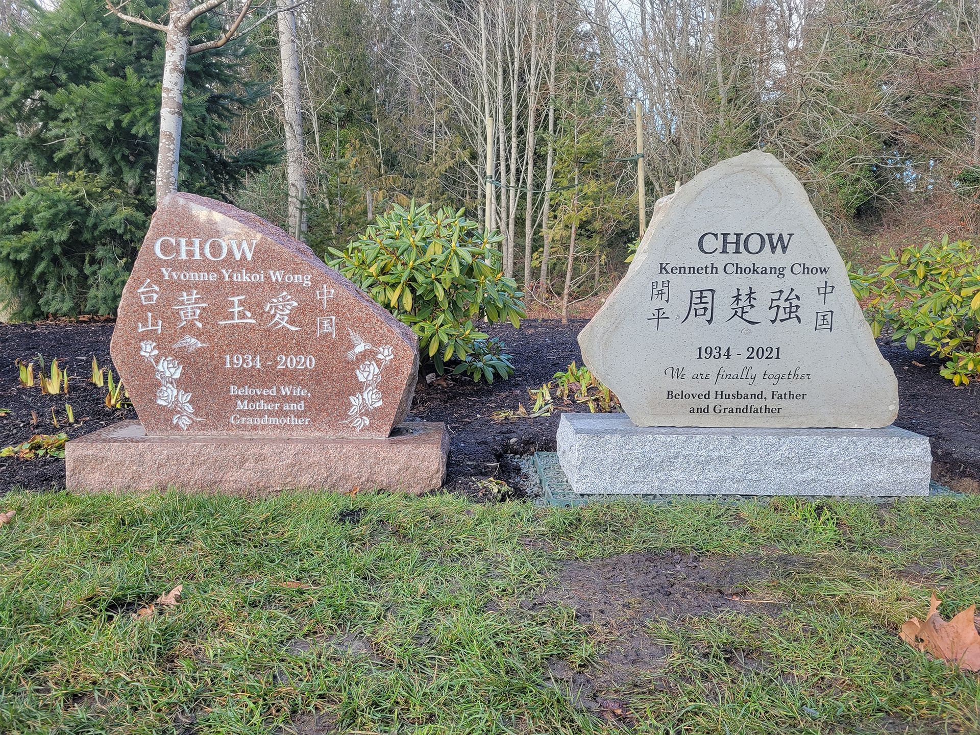 two gravestones in a cemetery with trees in the background .