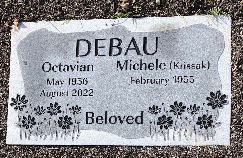 a gravestone for a person named debau with flowers on it .