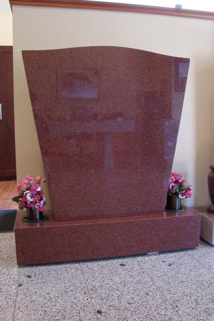 a red granite gravestone with flowers in vases in front of it .