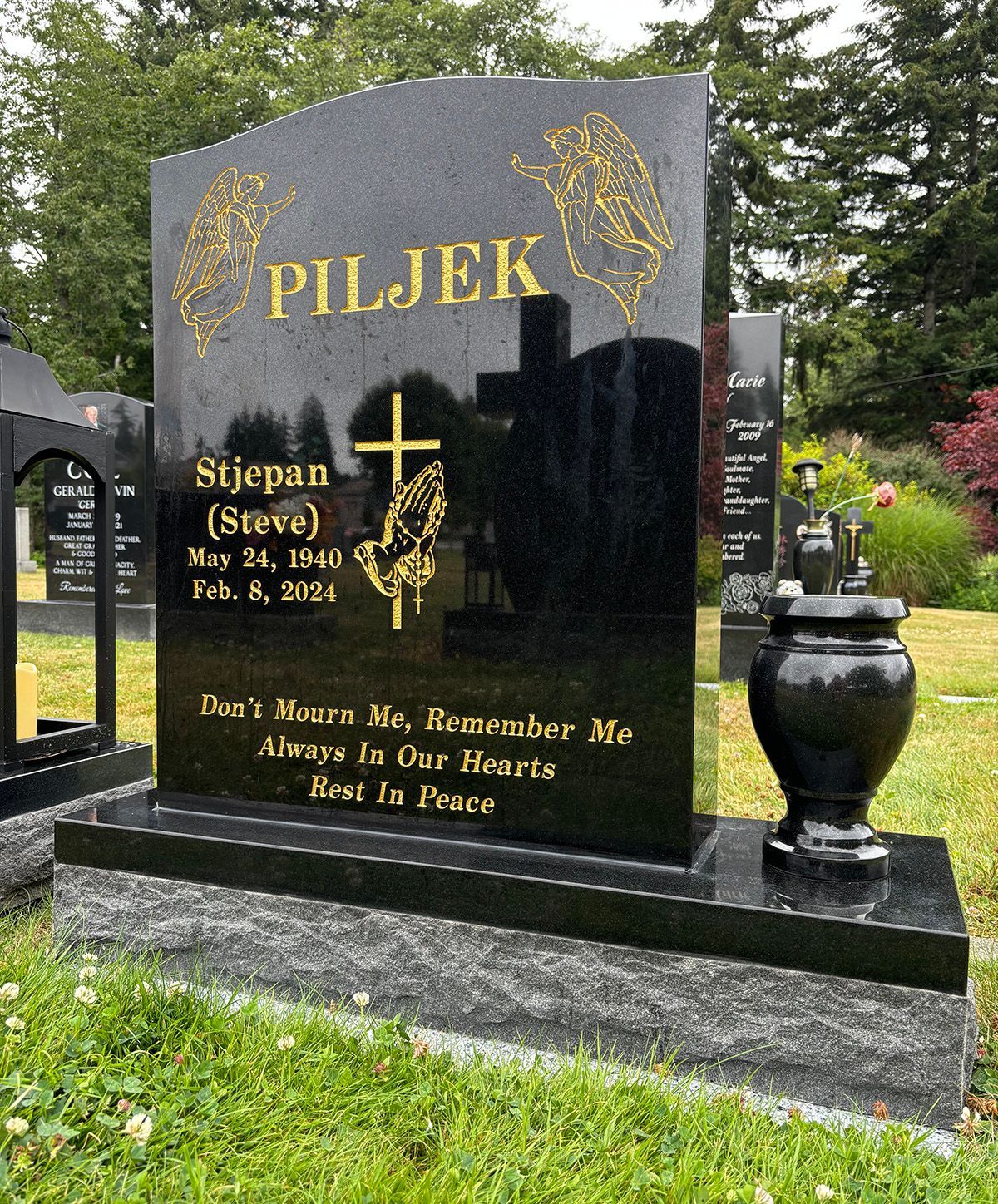 A photo of an ebony black granite upright memorial marker with gold paint. Featuring detailed engraving of angels, cross and praying hands with rosary