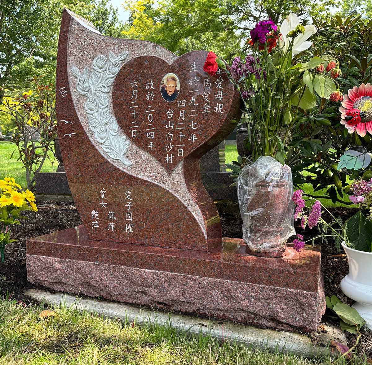 photo of a custom heart shaped memorial marker with carved roses. Made of pacific red granite sitting on a red granite base 