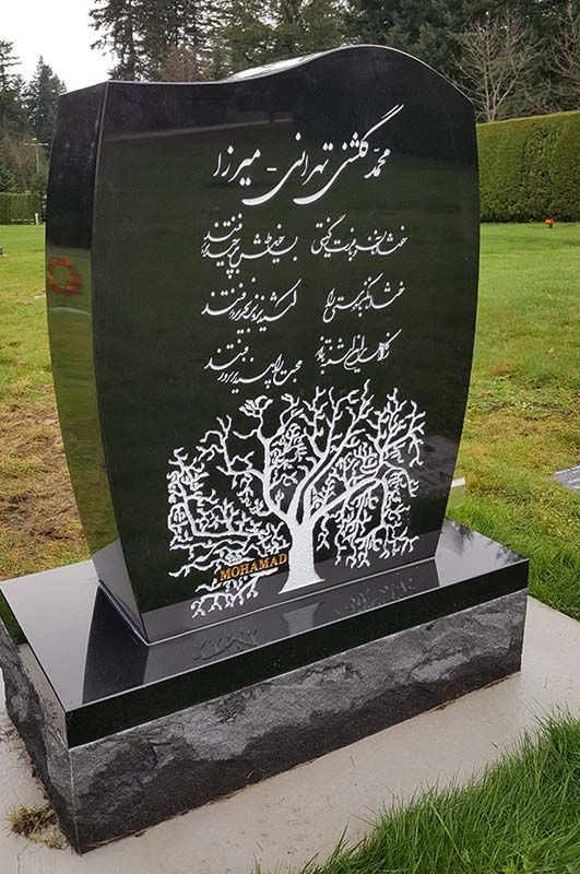 A black gravestone with a tree on it in a cemetery.