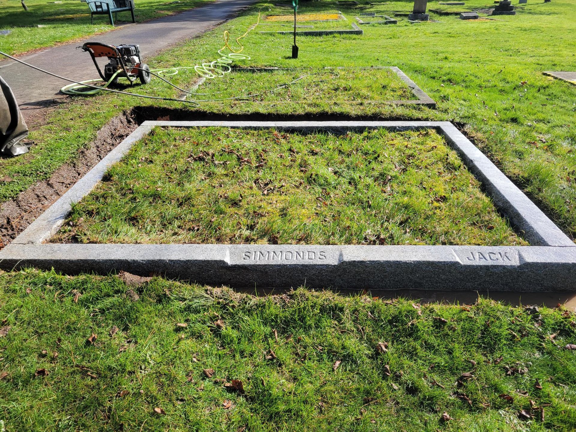 a grave in a cemetery with a gravestone in the middle of the grass .