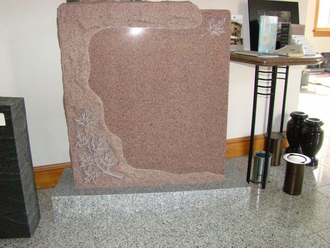 A pink granite headstone is sitting on a granite pedestal in a room.