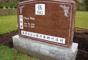 a red granite gravestone with chinese writing on it is in a cemetery .