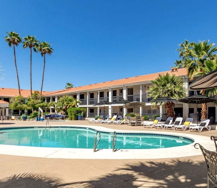 A large swimming pool in front of a hotel with palm trees.