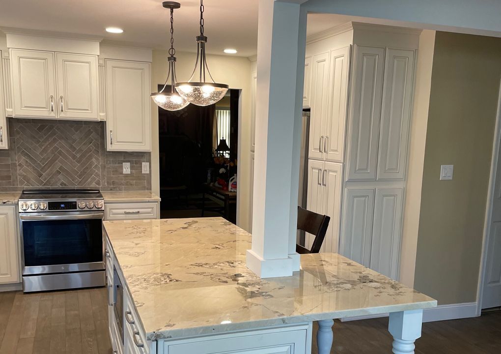 Bright kitchen with white cabinets, island with granite countertop, and pendant lights.