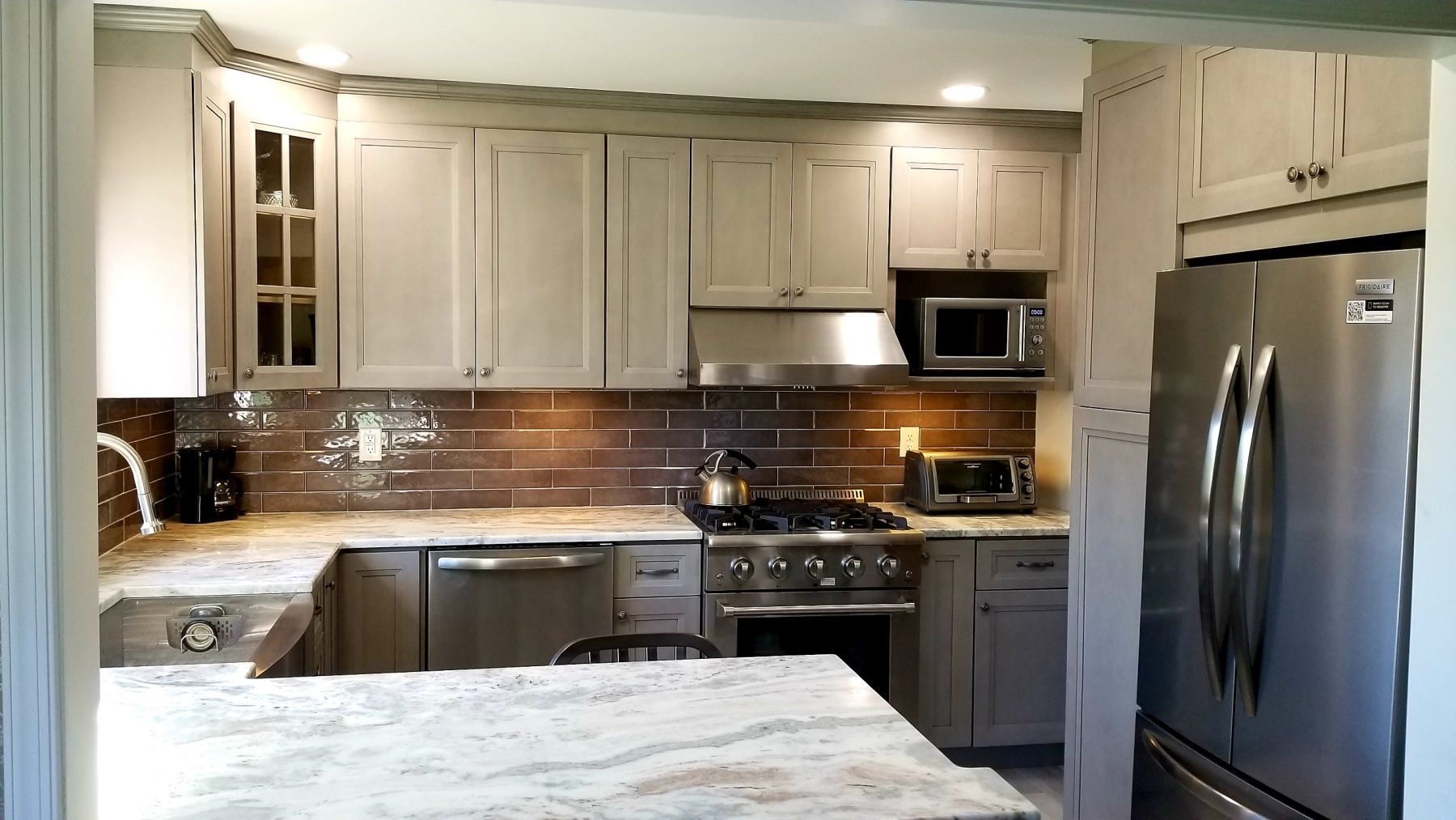 Kitchen with light gray cabinets, stainless steel appliances, and brown tiled backsplash.