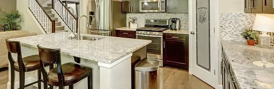 A well-lit kitchen with a large island, stools, and appliances, including a stove, microwave, and dishwasher.