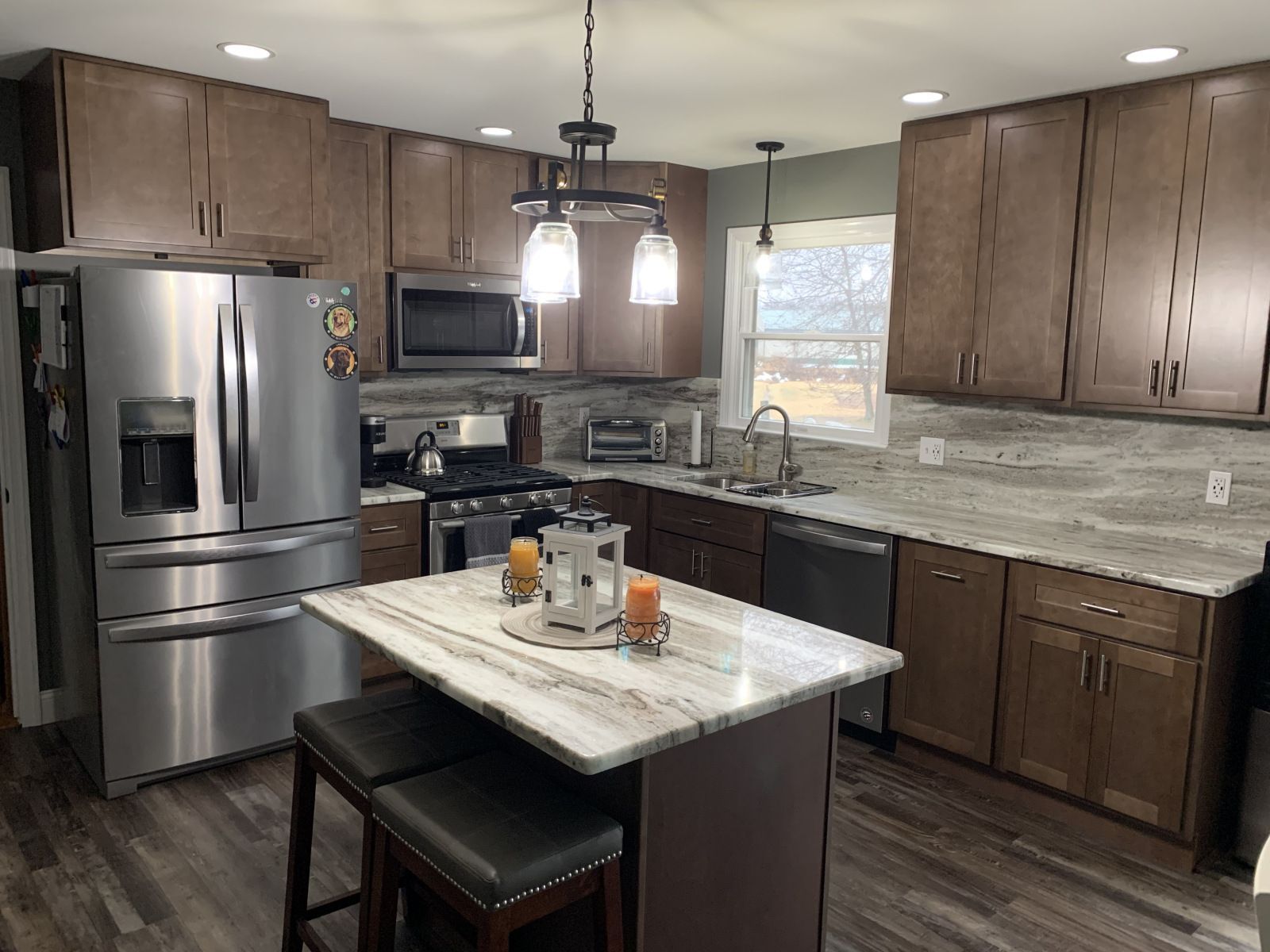 A kitchen with dark brown cabinets, stainless steel appliances, and a marble countertop island.