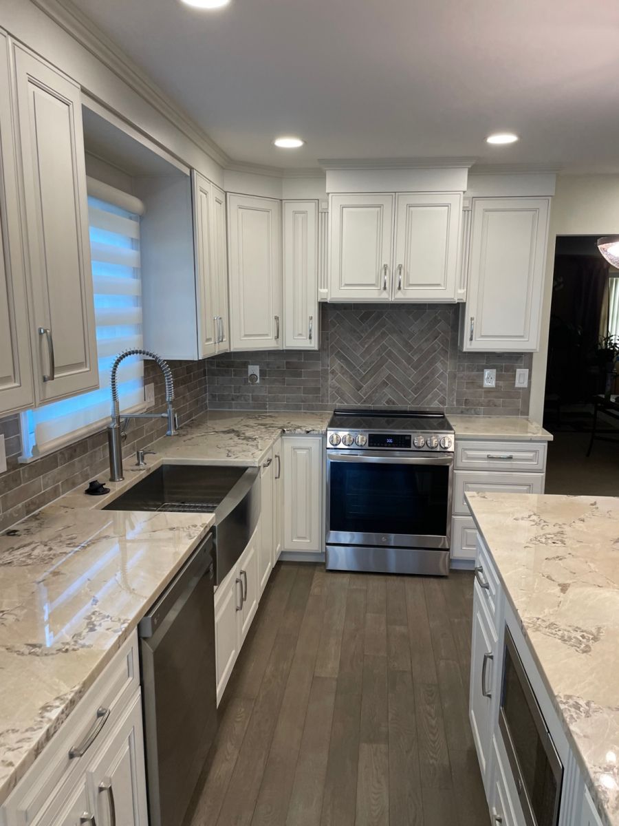 White kitchen with stainless steel appliances, granite countertops, and wood flooring.