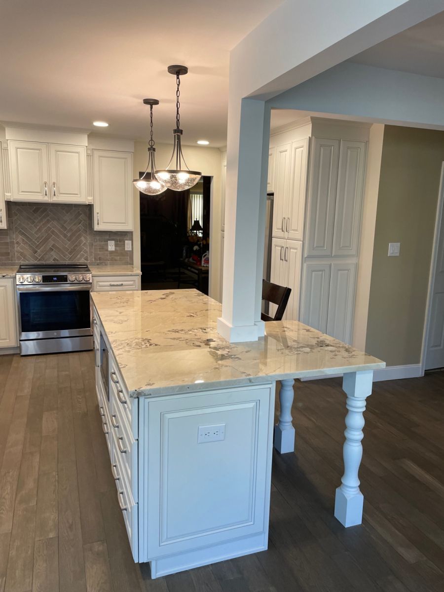 Kitchen with white cabinets, island with granite countertop, wood floors.