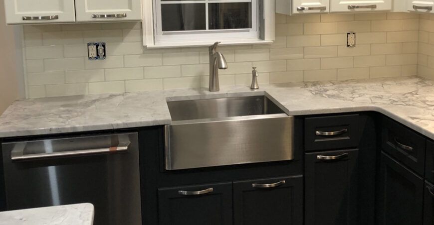 Kitchen with stainless steel sink, black and white cabinets, and white tile backsplash.