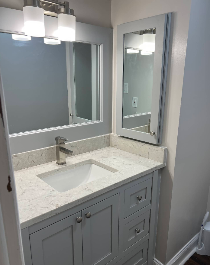 Bathroom vanity with a light gray cabinet, white countertop, and mirror.