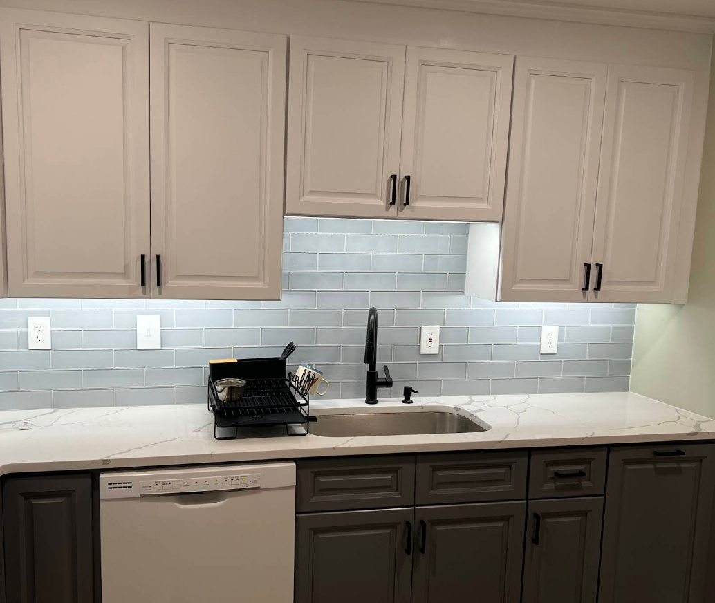 Kitchen with gray and white cabinets, stainless steel sink, and blue tile backsplash.