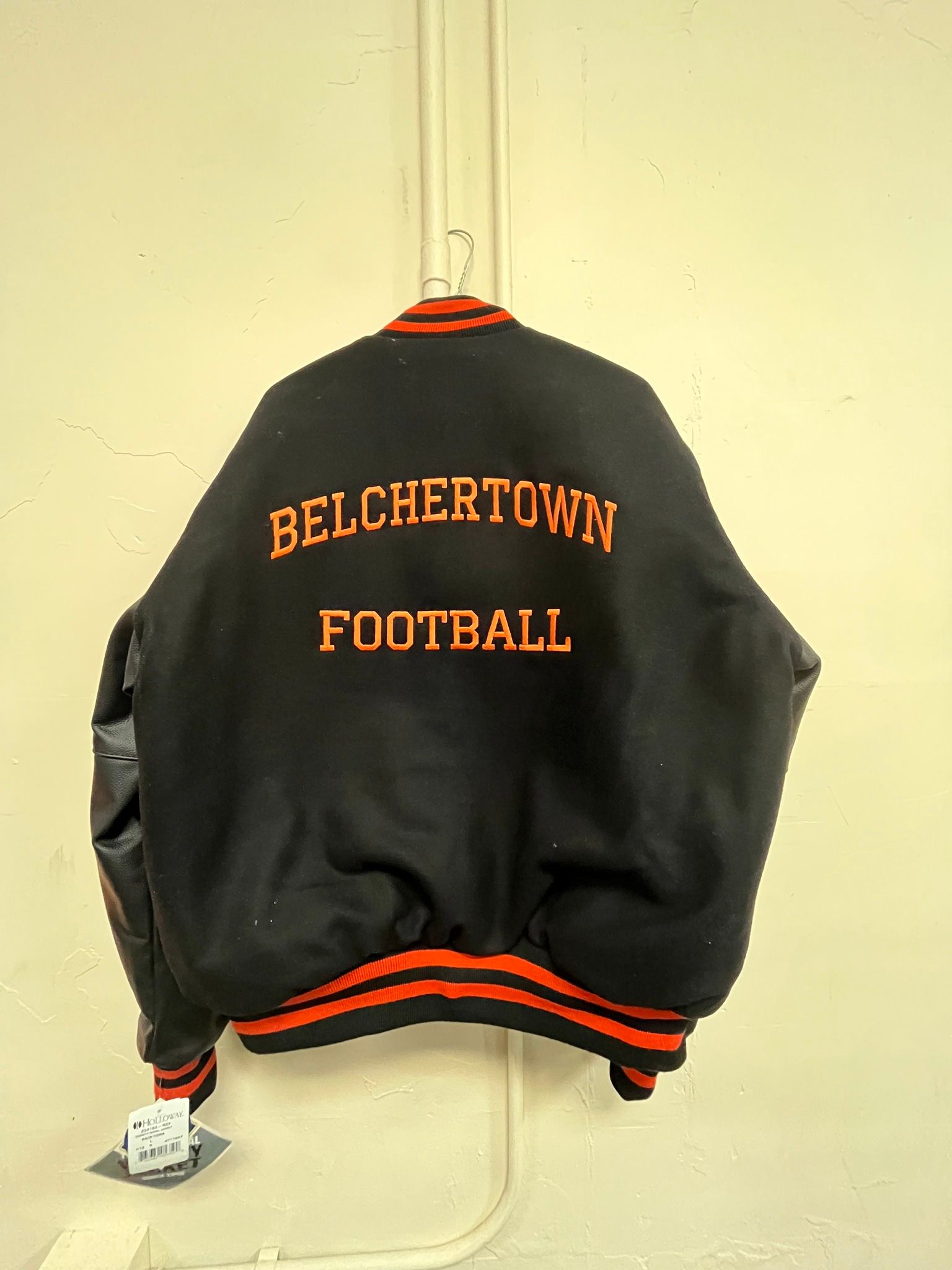 Black and orange Belchertown Football letterman jacket hanging on a hook.