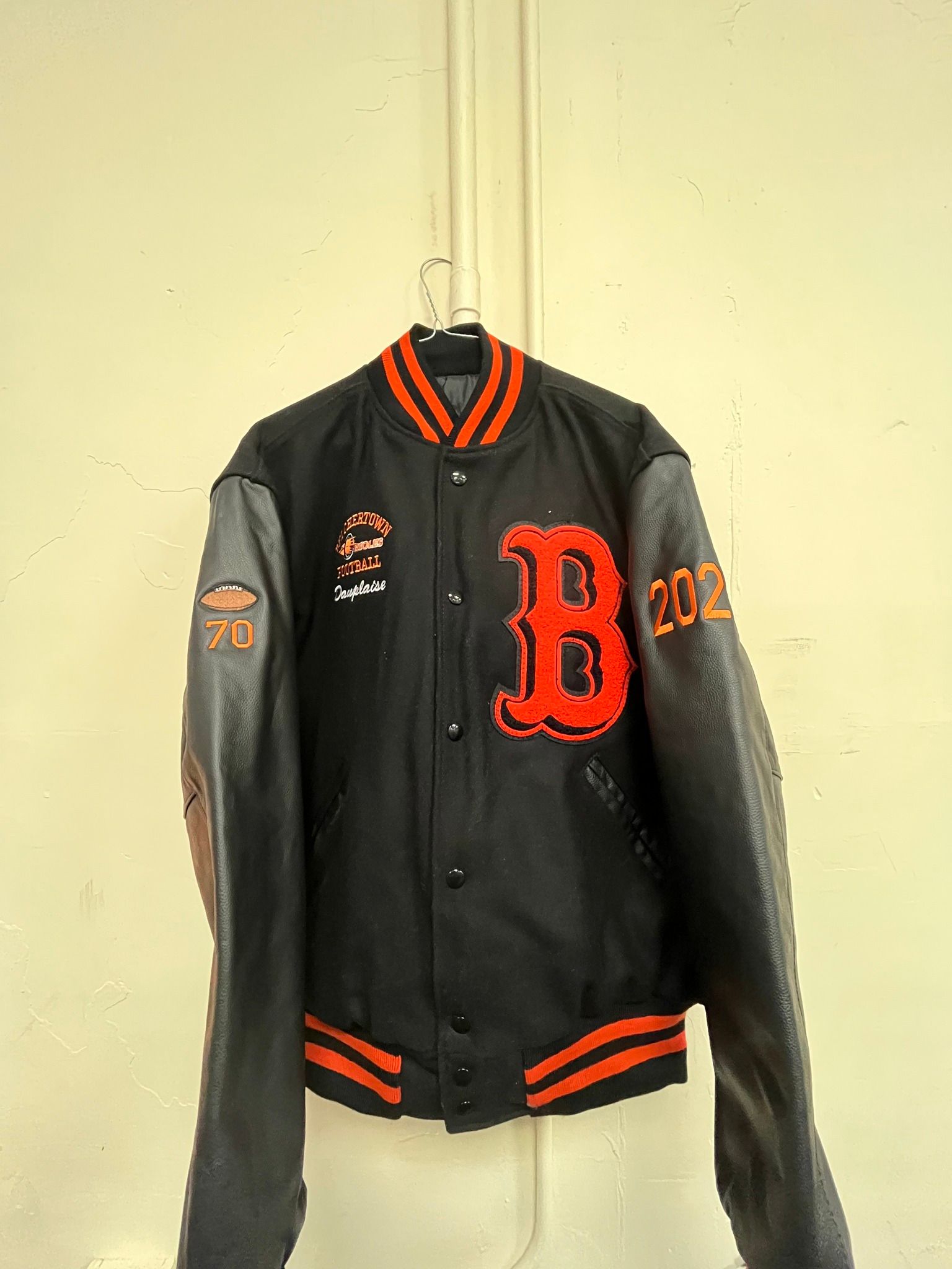 Black and orange varsity jacket hanging on a hook, with a large red 
