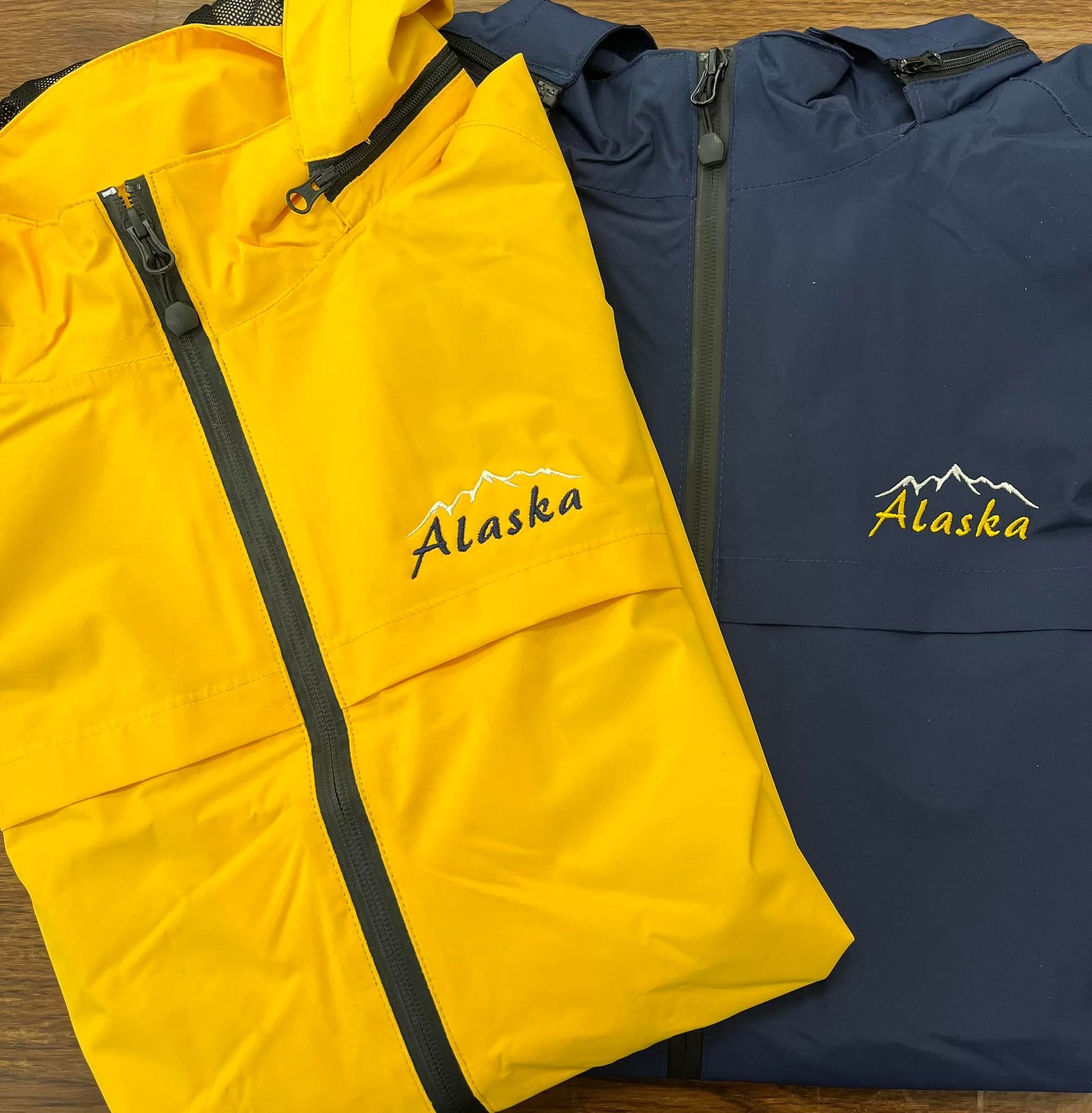 Two Alaska jackets, yellow and navy blue, side-by-side, zipped up, with mountain logo.