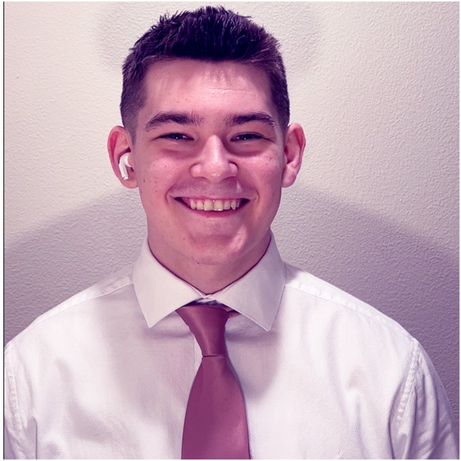 A man wearing a white shirt and a pink tie smiles for the camera