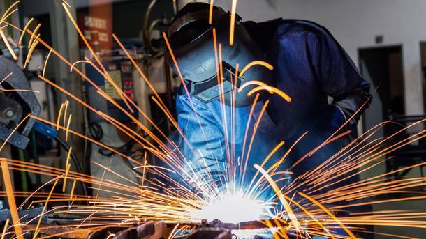 A man is welding a piece of metal in a factory.