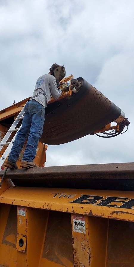A man is welding a piece of metal on top of a dump truck.