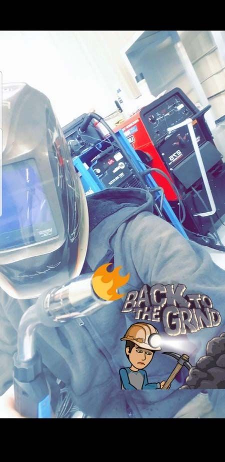 A man wearing a welding helmet is standing in front of a machine.