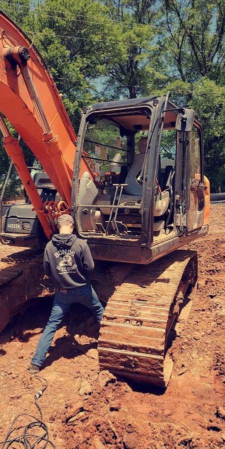 A man is standing next to a large excavator in the dirt.