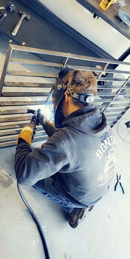 A man is welding a metal fence in a garage.