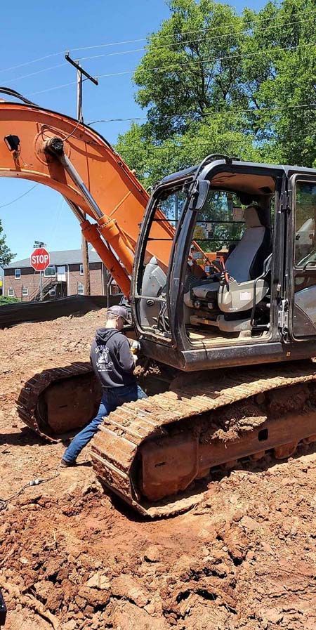 A man is standing next to a large excavator in the dirt.