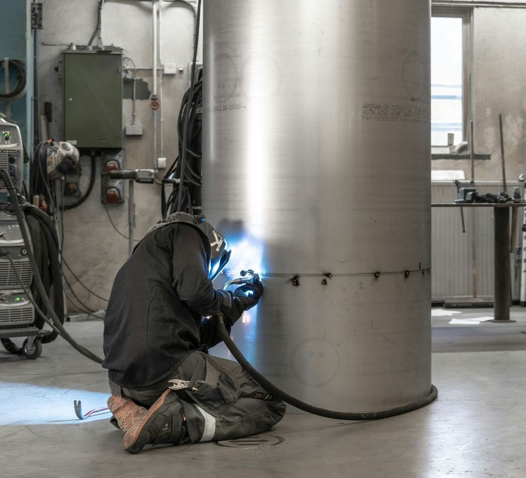 A man is welding a stainless steel pipe in a factory.
