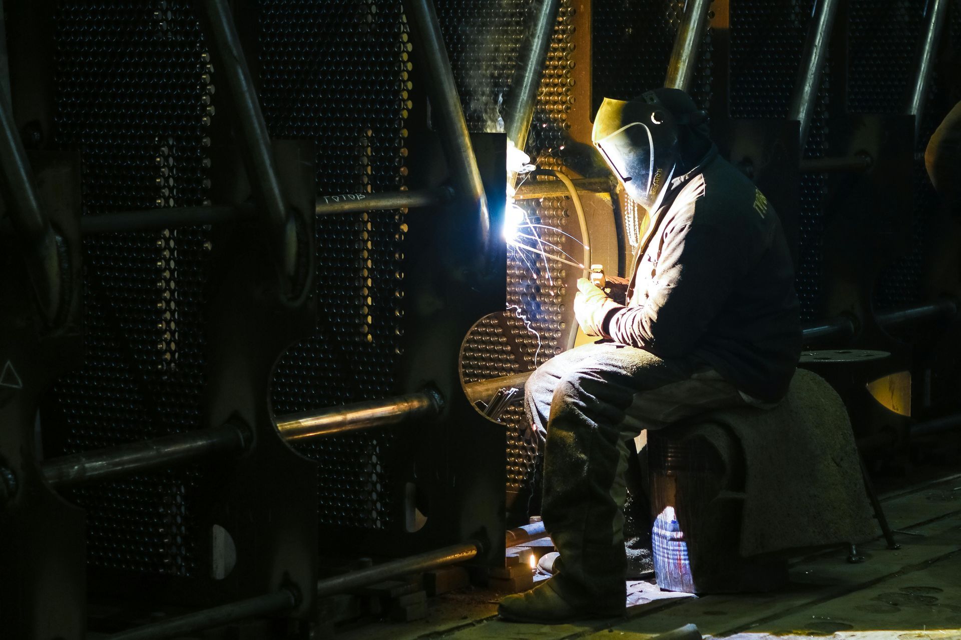 A man is welding a piece of metal in a dark room.