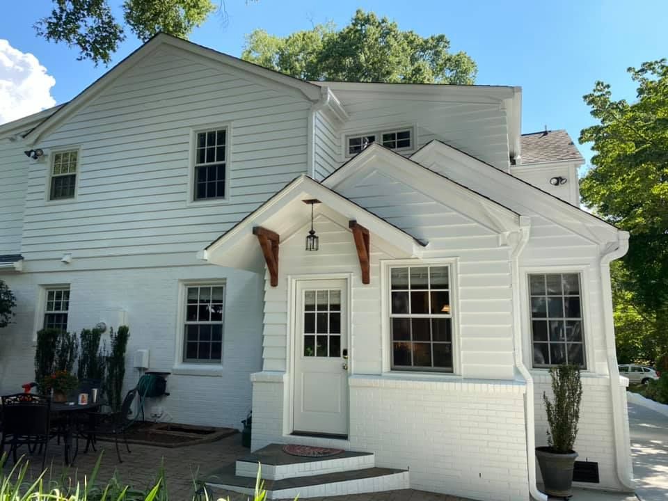 White house with a porch, door, windows, and a brick foundation under a blue sky.