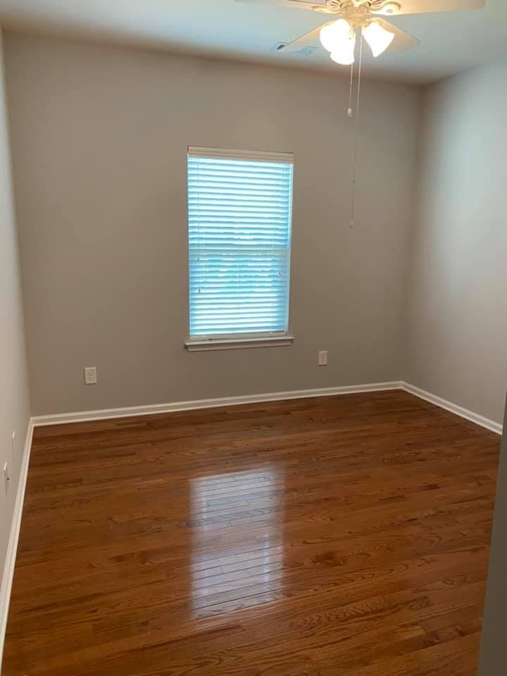 Empty room with hardwood floors, beige walls, a window with blinds, and a ceiling fan.
