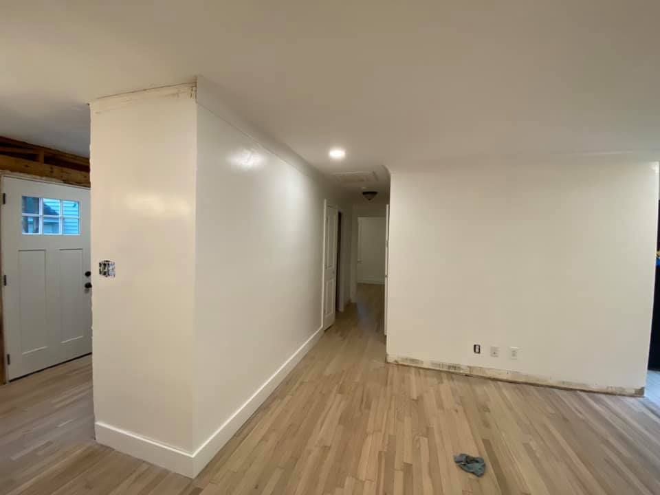 Interior view: white-painted walls, light wood floors, hallway, and a doorway.