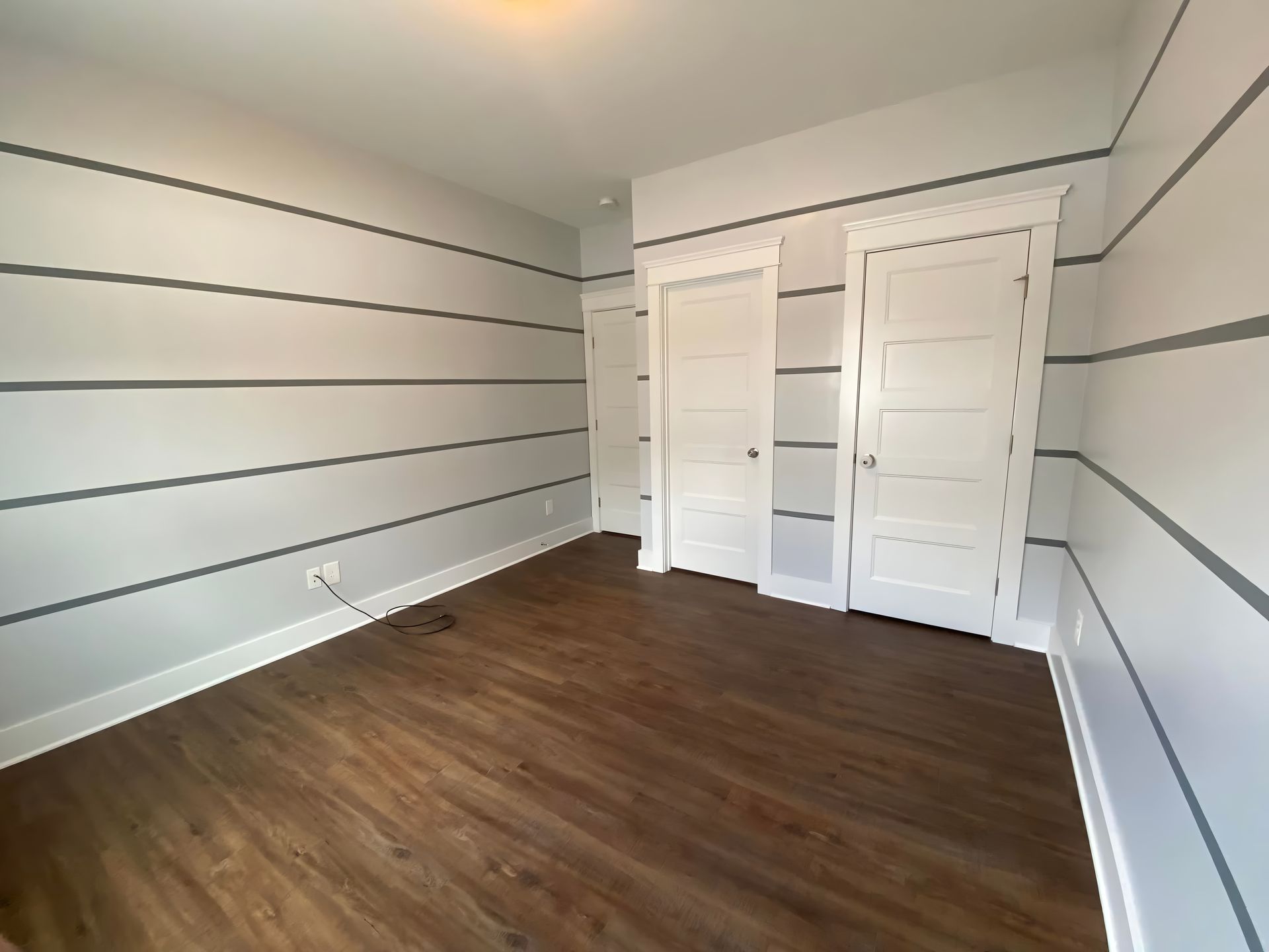 Empty room with gray striped walls, two white doors, and dark wood floors.