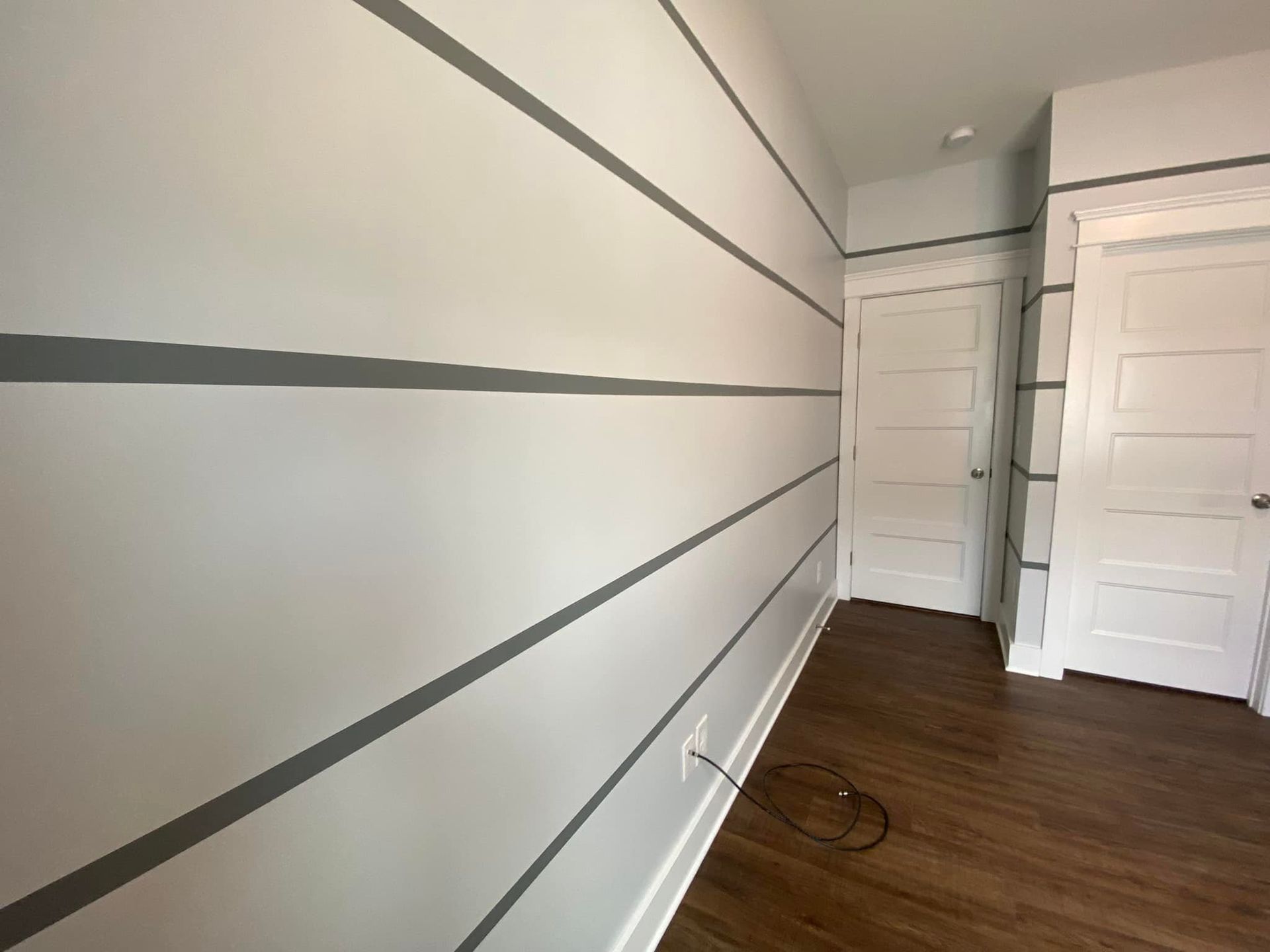 Gray-striped white walls in a room with wood floor, white doors and trim.