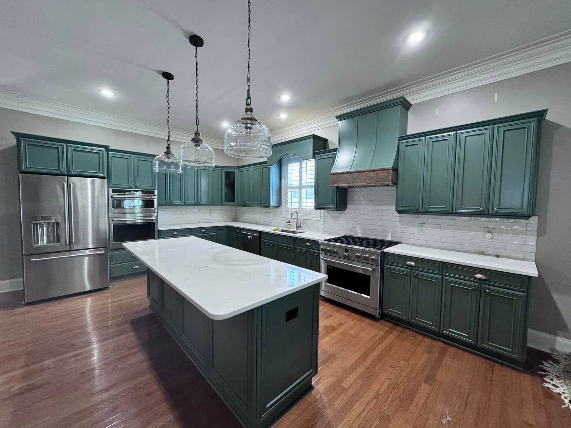 Green kitchen with stainless steel appliances, white countertops, and wooden floors.