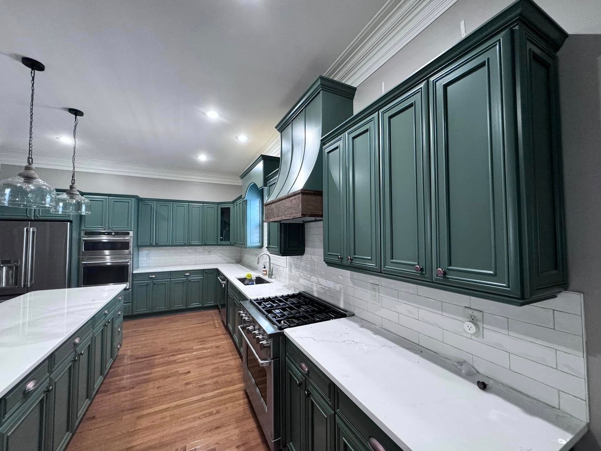 Green kitchen with white countertops, stainless steel appliances, and wood floors.