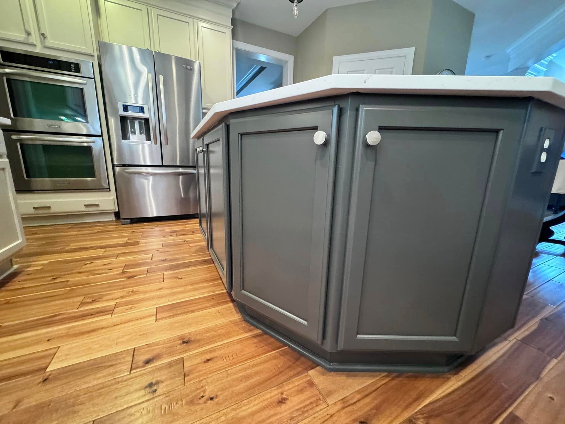 A kitchen with a gray island and wooden floor. Stainless steel refrigerator and oven visible.