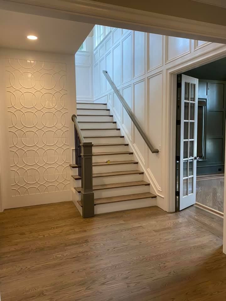 Entryway with staircase, patterned white wall, light wood floors, and open doorway.